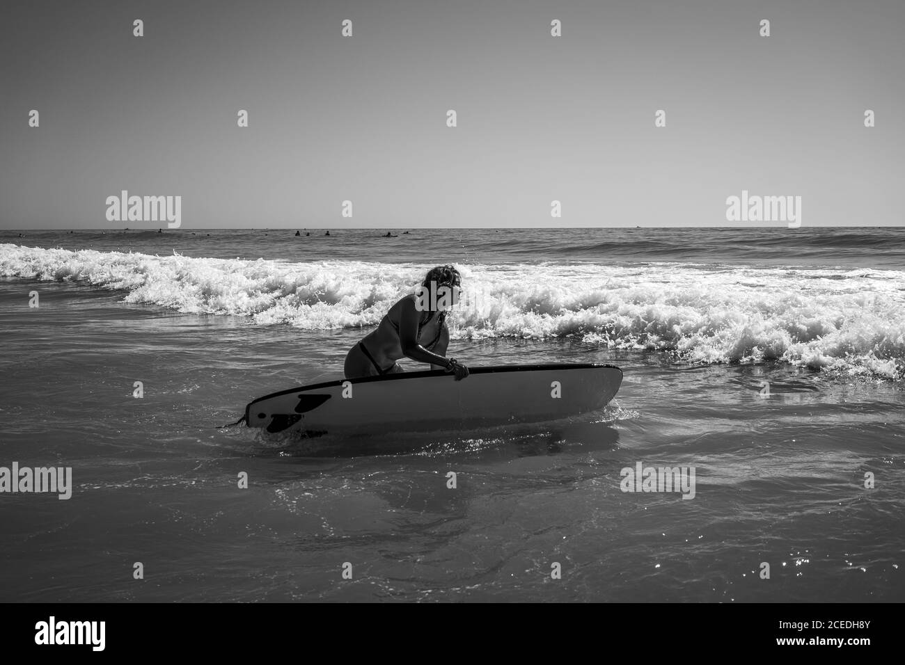 Graustufenaufnahme einer kaukasischen Frau, die am Wellenmeer surft In Cadiz Stockfoto