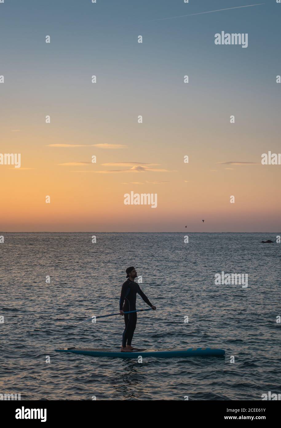 Mann übt Paddelsurfen mit Neopren bei Sonnenaufgang an einem paradiesischen Strand Stockfoto