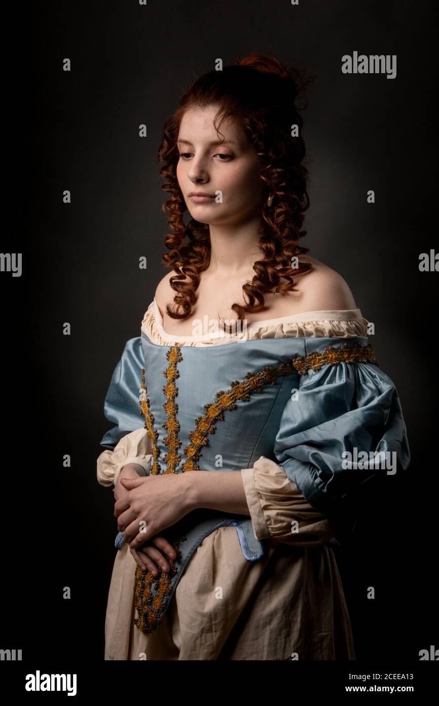 Attraktive junge Dame in wunderschönen barocken Kleid halten die Hände auf Bauch beim Stehen auf schwarzem Hintergrund Stockfoto