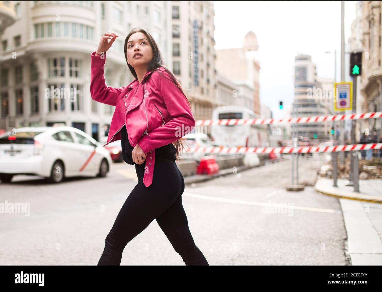 Seitenansicht der modernen schlanken Frau in rosa Lederjacke Straße überqueren und wegschauen Stockfoto