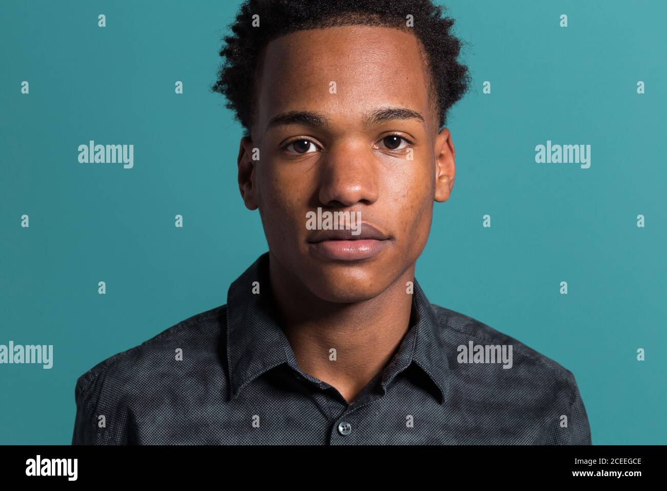 Crop Porträt von jungen afroamerikanischen ernsten Mann im Hemd suchen Bei der Kamera auf blauem Hintergrund Stockfoto
