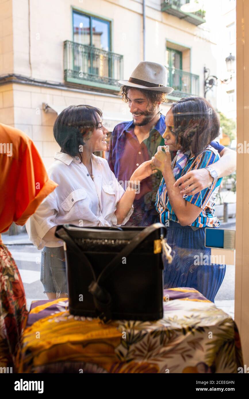 Junge Männer und Frauen lächeln und schauen sich die Kleidung im Inneren an Kleiner Laden, während man auf der Straße in der Nähe des Schaufensters steht Stockfoto