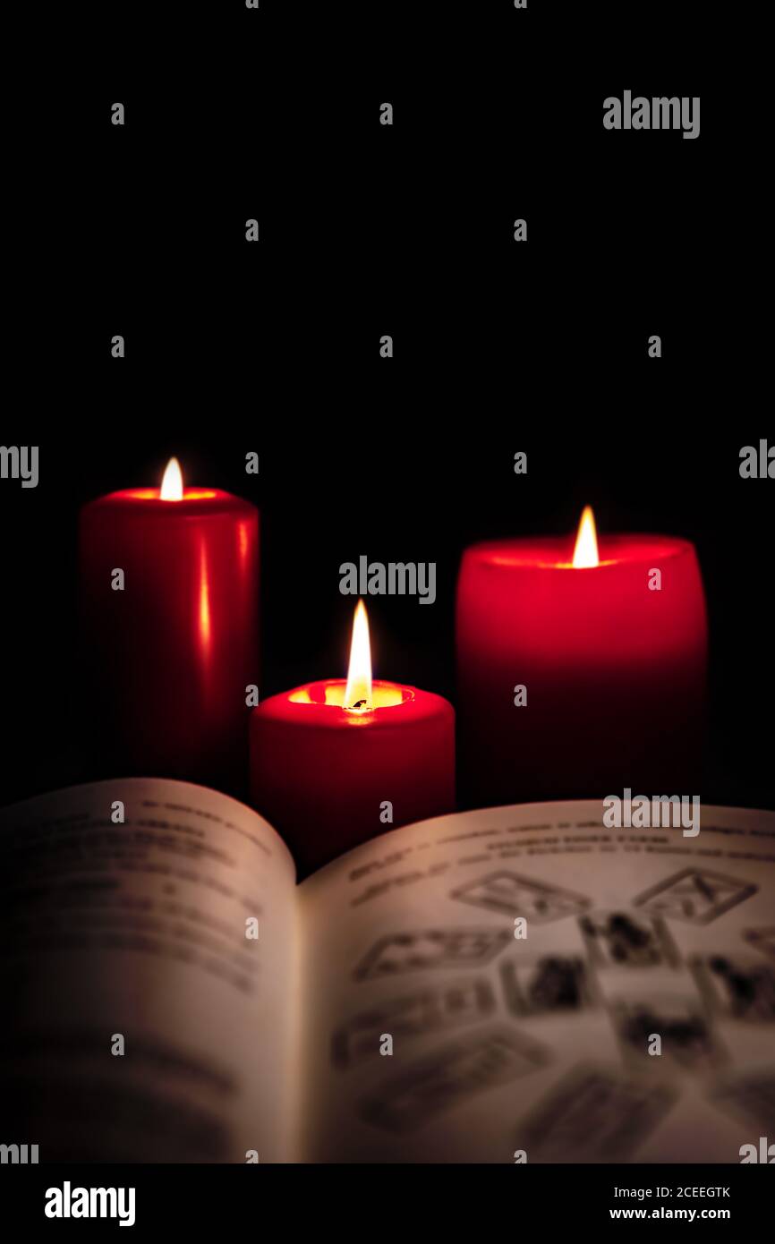 Altes Buch mit Tarot-Karten und roten Kerzen vor schwarzem Hintergrund, Horoskop und Glück lesen, Copyspace Stockfoto