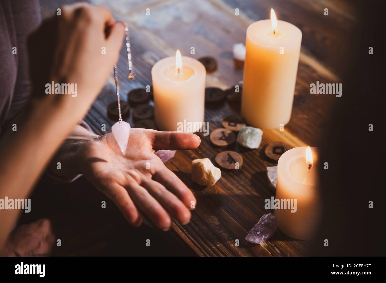 Librate mit einem Pendel über der Hand, Heilungs- oder orakelvorhersagenden, Kerzen, Runen und Heilsteine Stockfoto