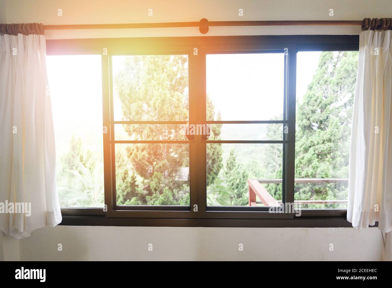 Schlafzimmer Fenster in der Morgen-/Sonnenlicht durch offene Vorhänge im Zimmer mit Balkon und Natur Baum vor dem Fenster Stockfoto