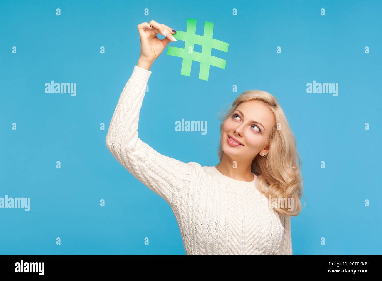 Schöne blonde Frau Blogger Blick auf Hashtag Zeichen sie hält über dem Kopf, beliebte Post im Internet, einfache Suche. Innenaufnahme des Studios isoliert auf BL Stockfoto