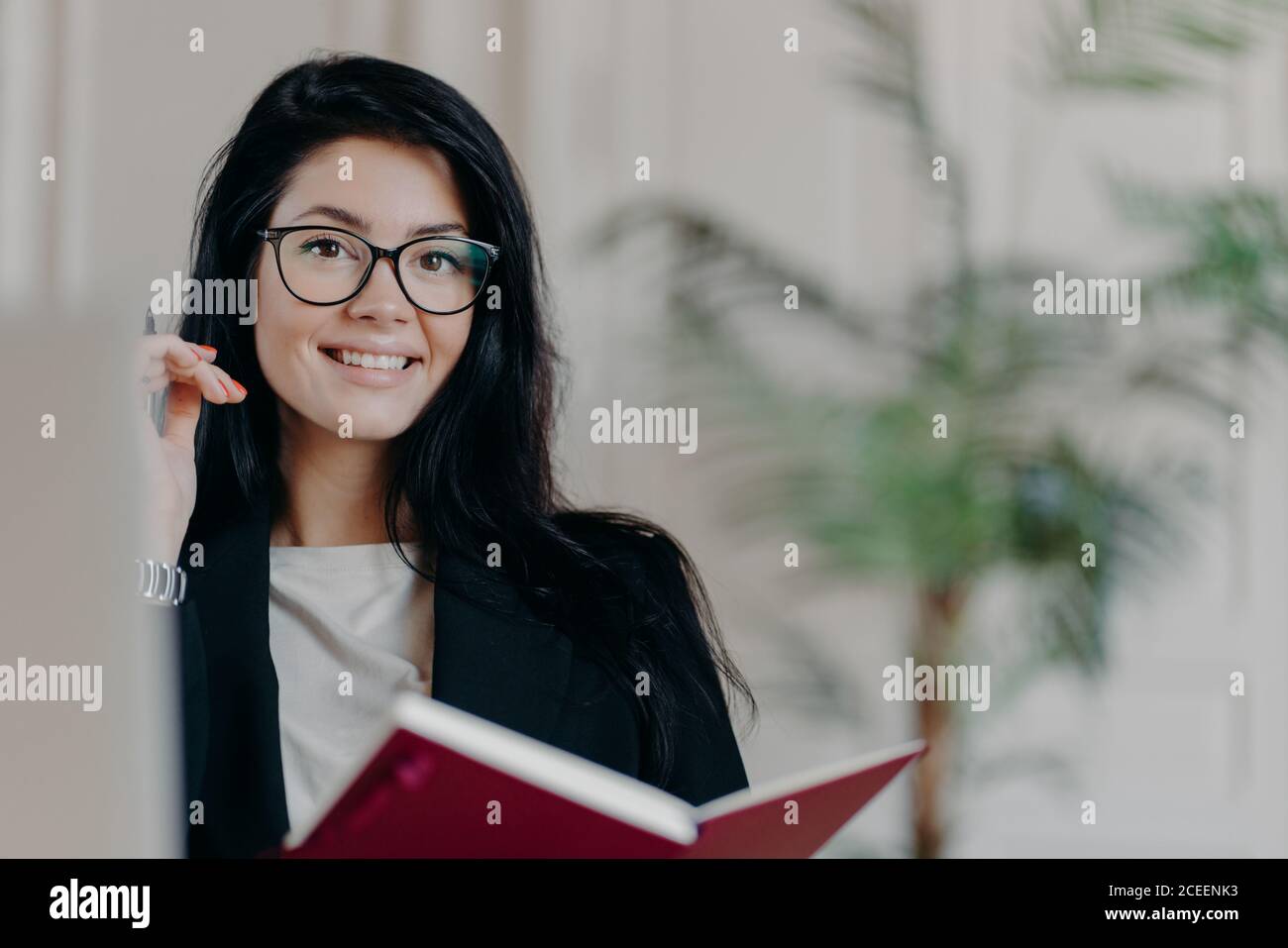 Horizontale Aufnahme von zufriedenen Brünette Freiberufler arbeitet aus der Ferne von zu Hause, hält Notizblock und Stift, macht Notizen, verbringt Freizeit für die Forschung, füllt ou Stockfoto