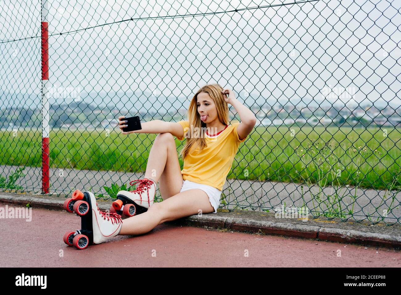 Teen Mädchen tragen Rollschuhe und zeigt zwei Finger auf Kamera des Smartphones Selfie auf der Straße. Stockfoto