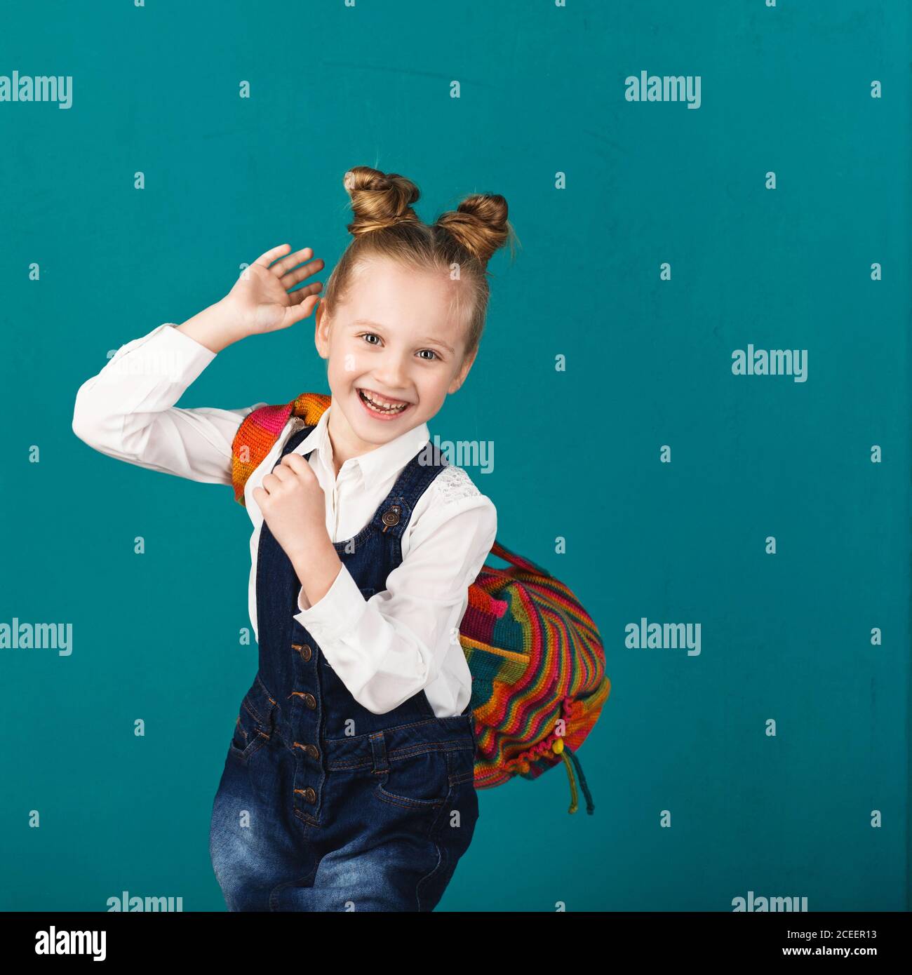 Lustige lächelnde kleine Mädchen mit großen Rucksack springen und Spaß an der blauen Wand. Blick auf die Kamera. Schulkonzept. Zurück zur Schule Stockfoto