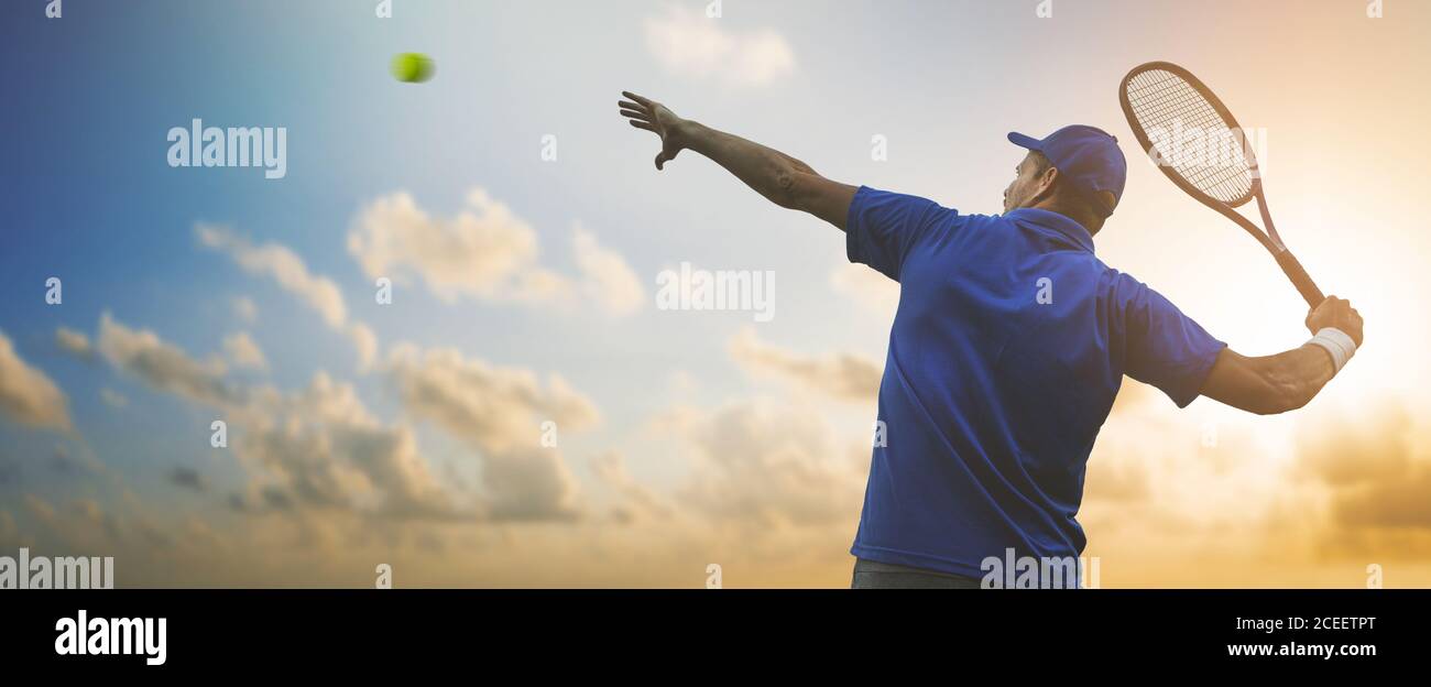 Professioneller männlicher Tennisspieler in blauem Hemd, der Ball mit Schläger auf Sonnenuntergang Himmel Hintergrund trifft. Banner Copy Space Stockfoto