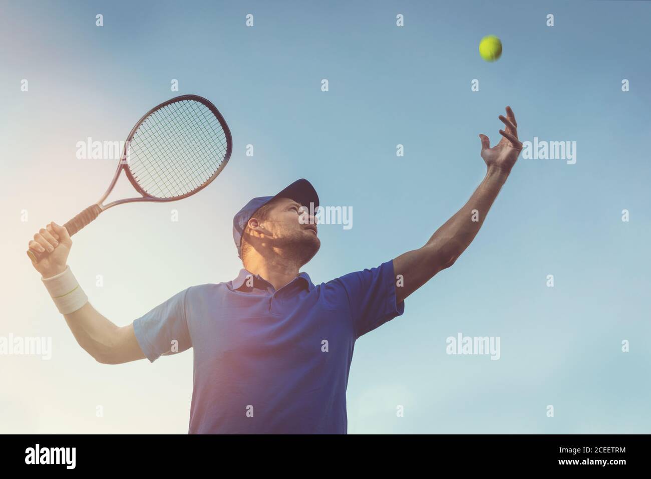 Aktiver junger Mann spielt Tennis im Freien. Servieren Sie den Ball gegen blauen Himmel Stockfoto