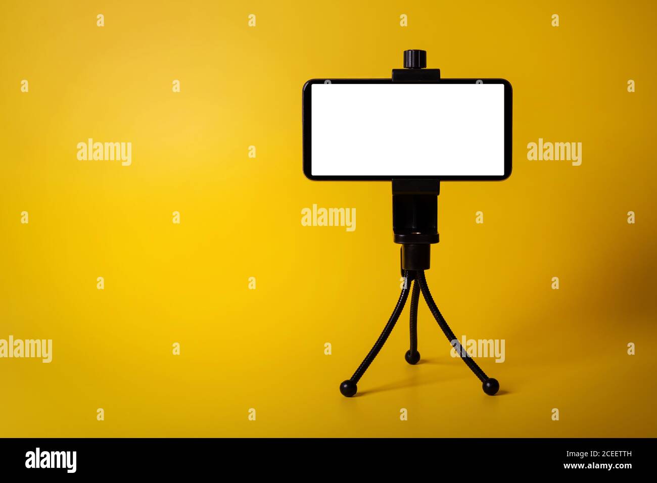 Mobiltelefon auf Mini-Stativ mit leerem Bildschirm isoliert auf gelbem Hintergrund montiert. Platz zum Kopieren Stockfoto