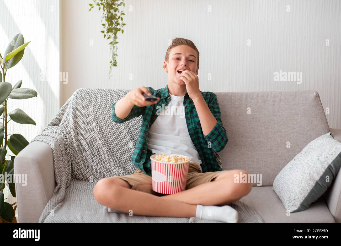 Fröhlicher Teenager, der allein Fernsehen schaut, Popcorn isst Stockfoto