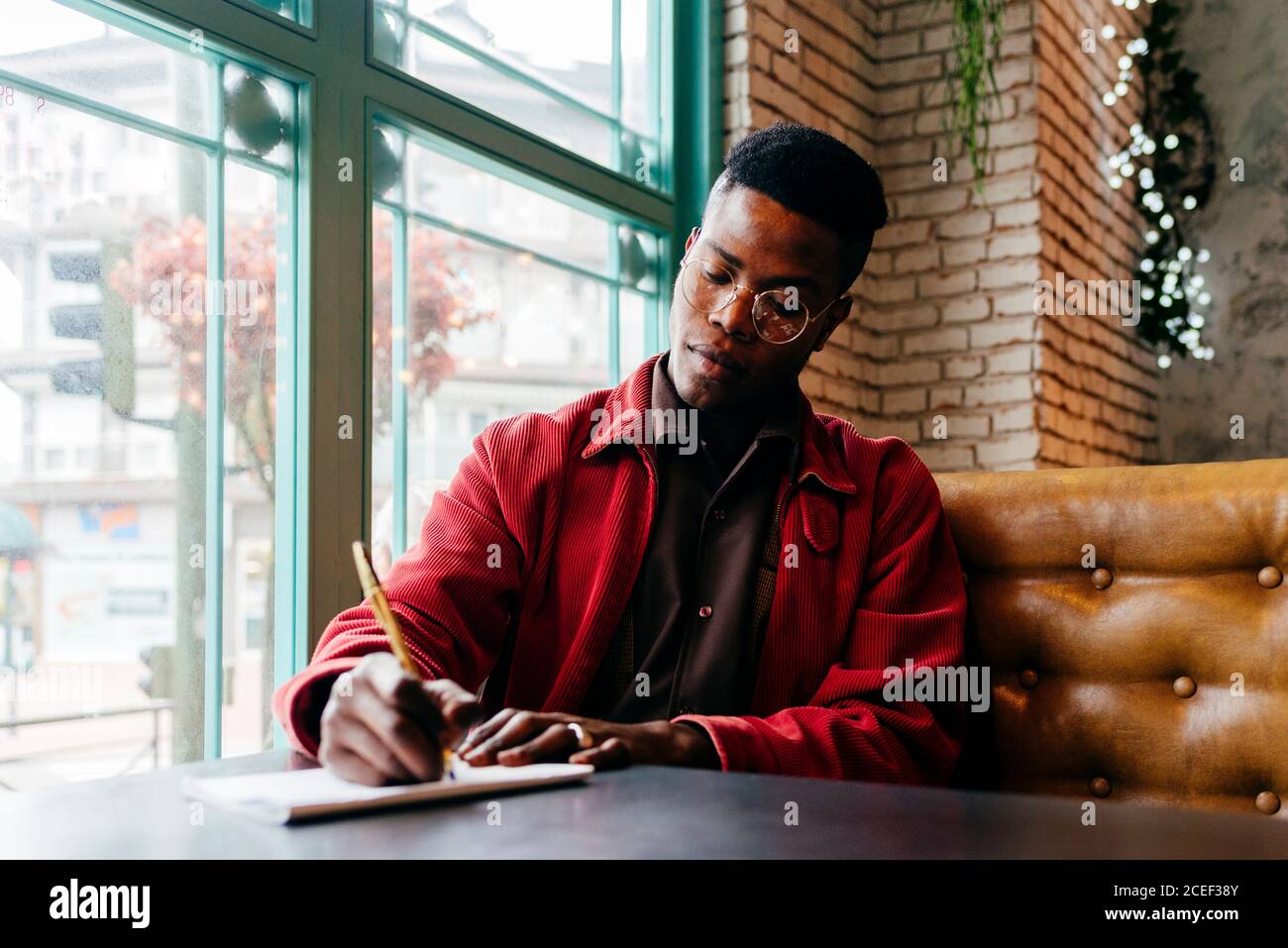 Serious african männlich in roter Jacke Brief am Tisch in Café Stockfoto