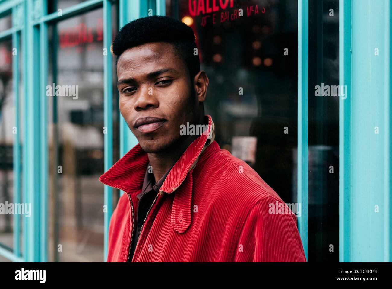 Stilvolle afrikanische männliche Putting Hands in der Tasche des roten Pullovers Stehen am Eingang zum Café Stockfoto