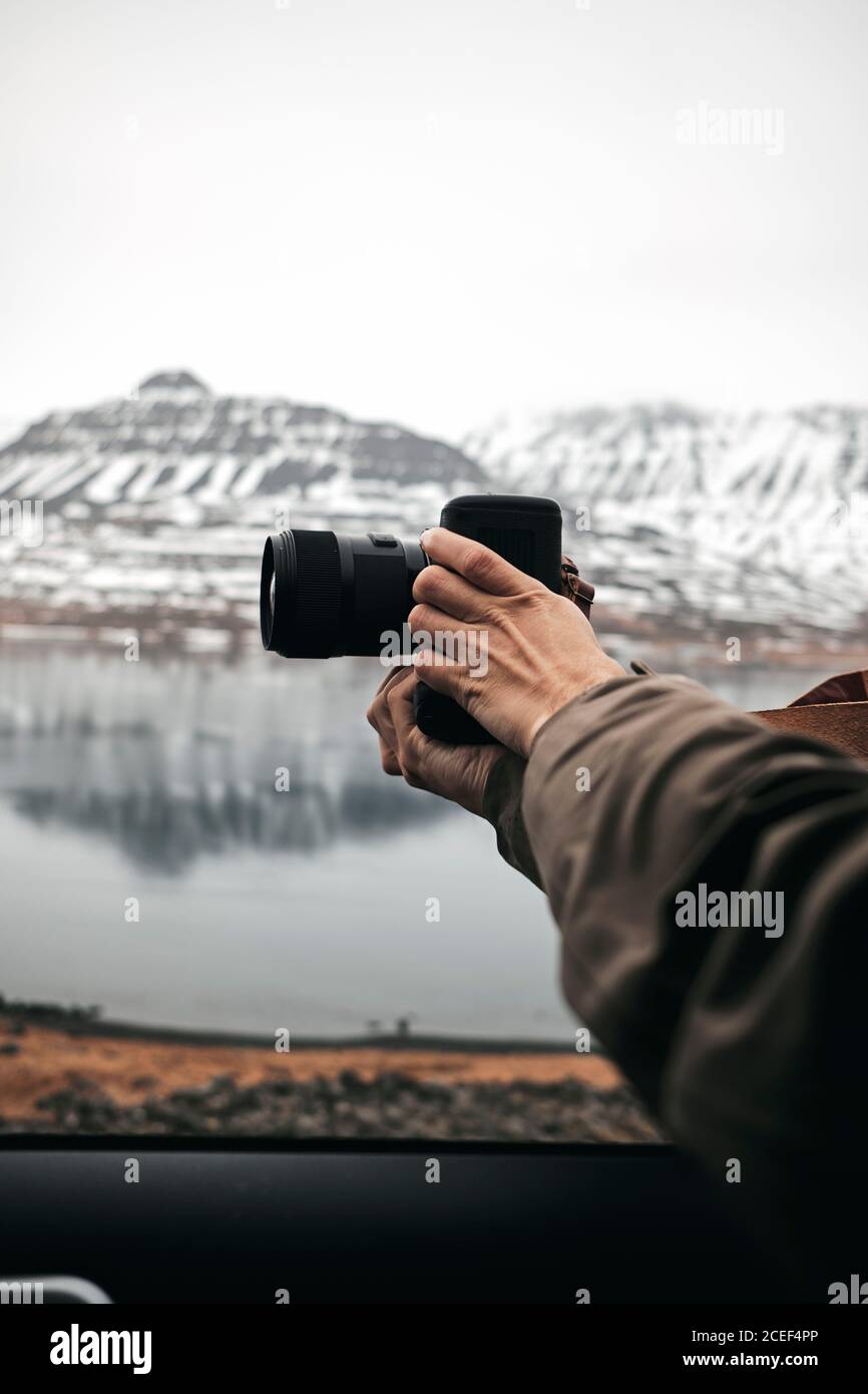 Seitenansicht des professionellen Ausschnittfotografen, der mit der Kamera fotografiert Am See in den Hügeln in Island Stockfoto