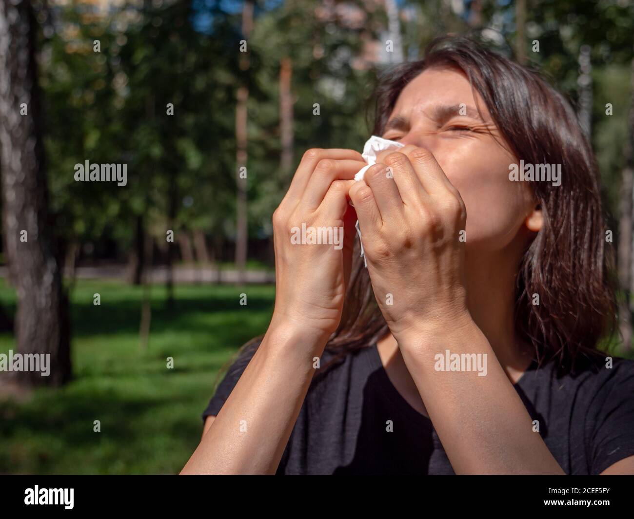 Frau mit geschlossenen Augen leiden unter Gras Pollen Allegry Niesen in Papiergewebe an einem sonnigen Tag im Park. Allergisches Nasenlaufkonzept. Stockfoto