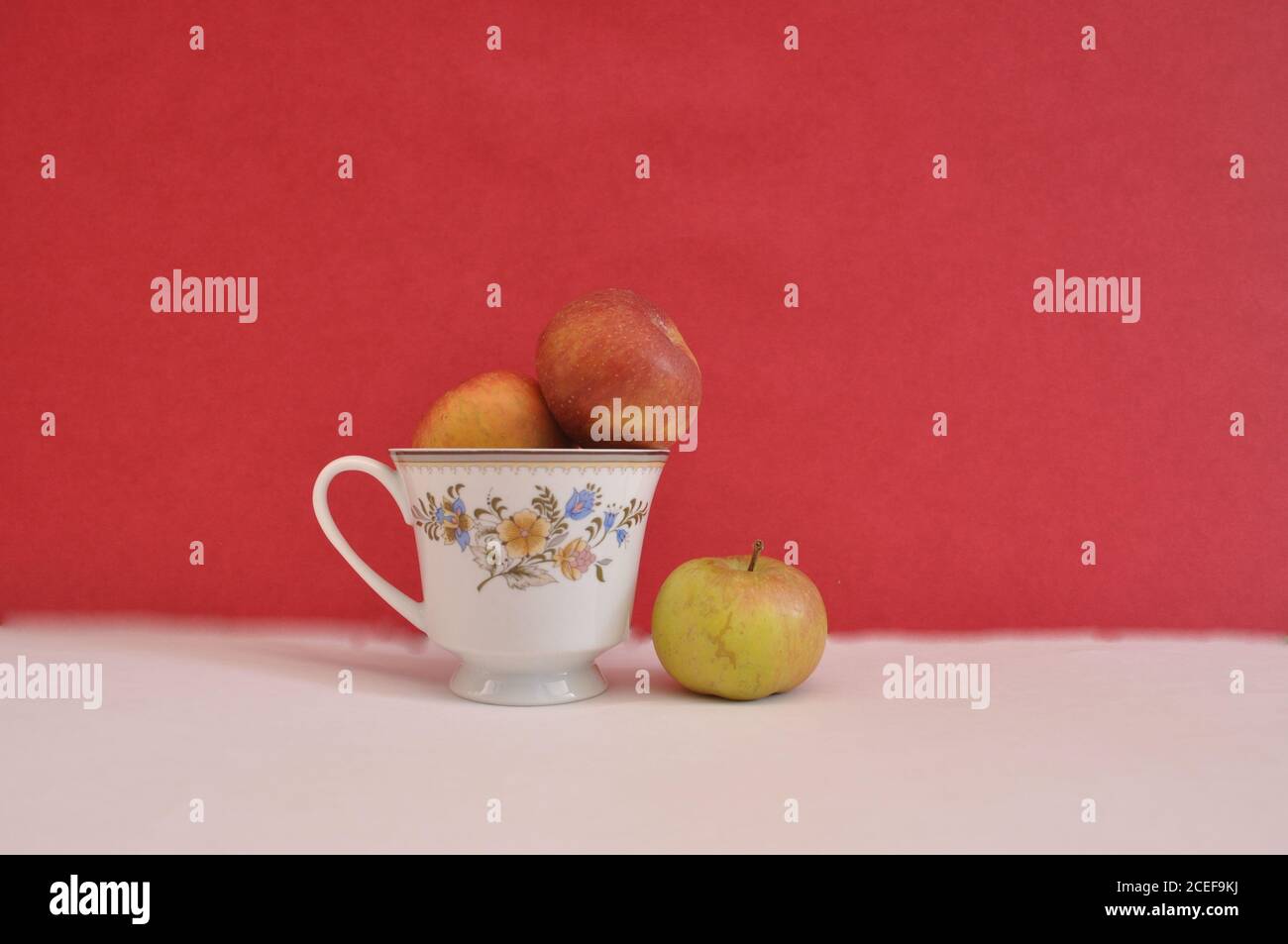 Kaffeetasse mit Blumenmotiven, mit frischen Äpfeln innen und außen, konzeptuelles Foto von Trennung, Trennung, auf weißem Grund und rotem Hintergrund Stockfoto