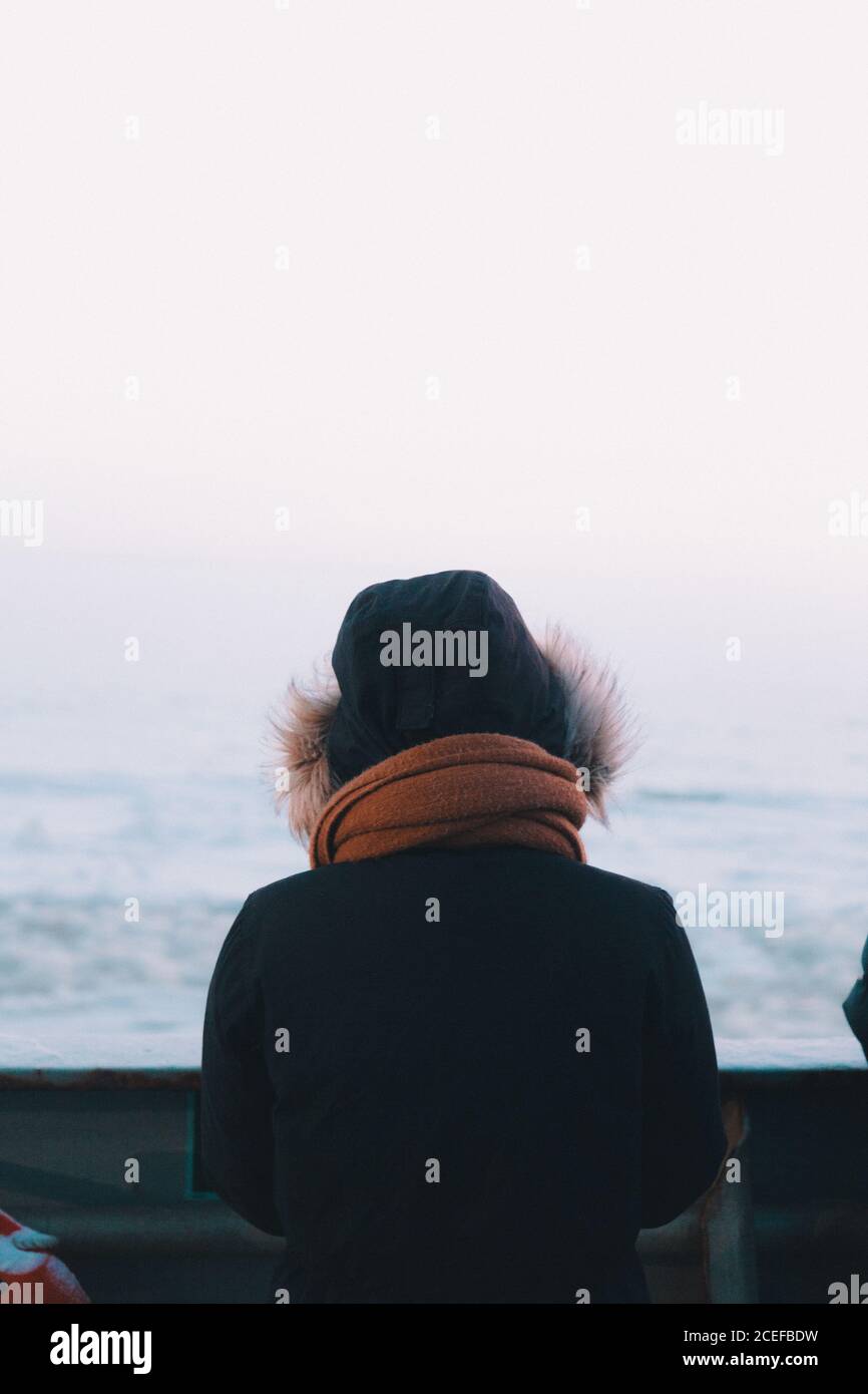 Rückansicht einer Frau im warmen Außenoutwear mit Kapuze, die auf Deck eines Schiffes steht, das im kalten Meer segelt Stockfoto