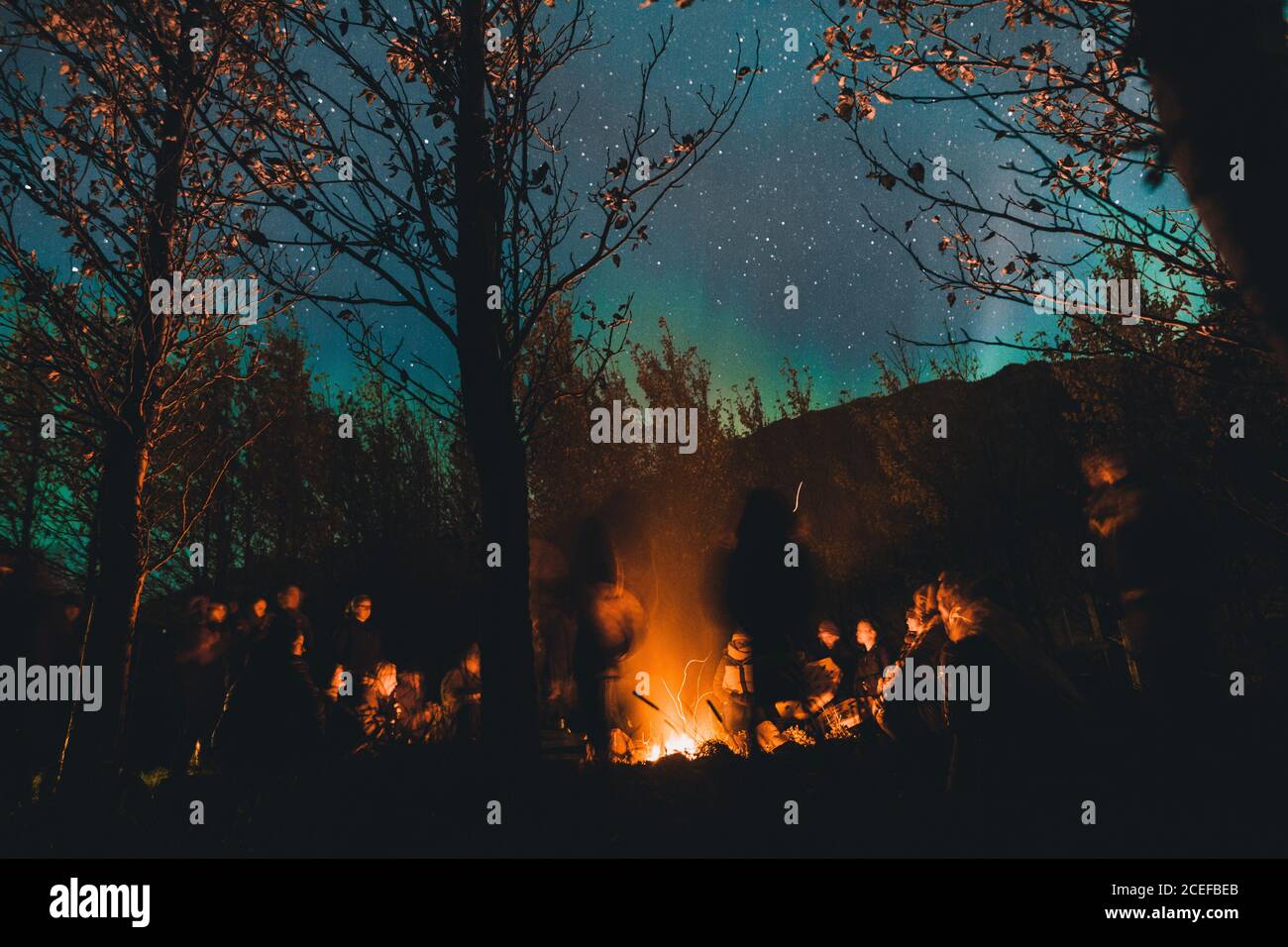 Gruppe von Menschen, die sich um Feuer im Wald versammeln Stockfoto