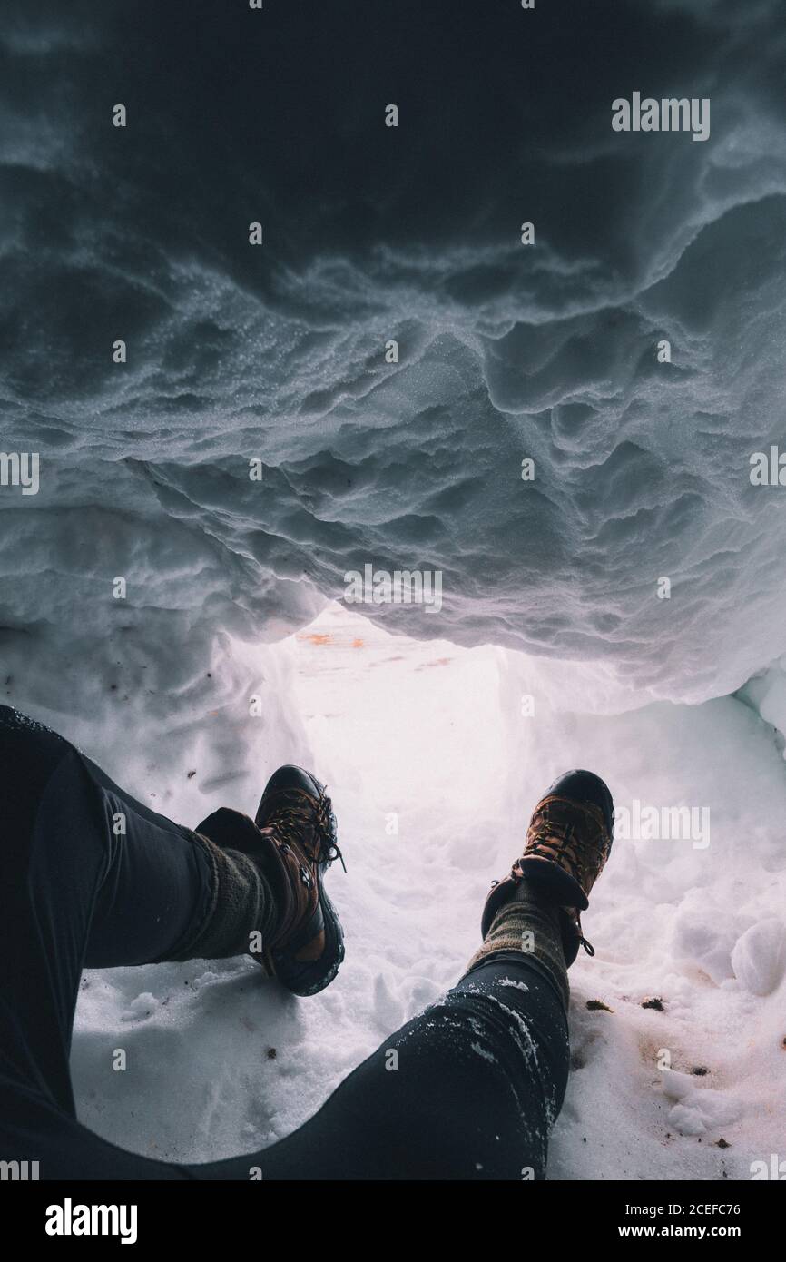 Kornaufnahme der Beine des Reisenden in Stiefeln, die im Schnee sitzen Höhle mit Licht unten Stockfoto