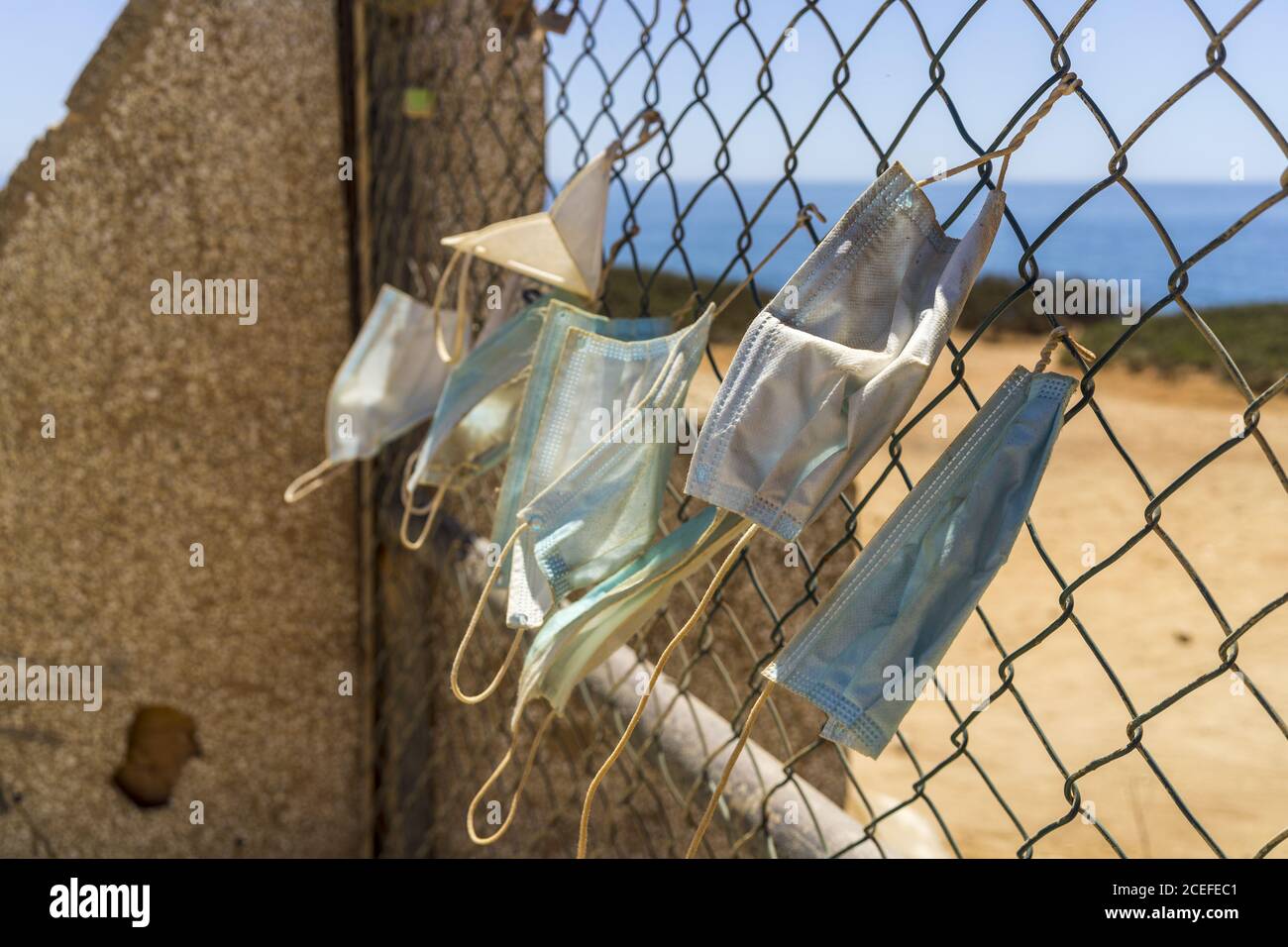 Nahaufnahme der verwendeten medizinischen Masken, die an das Eisen befestigt sind Netz in der Nähe des Strandes Stockfoto