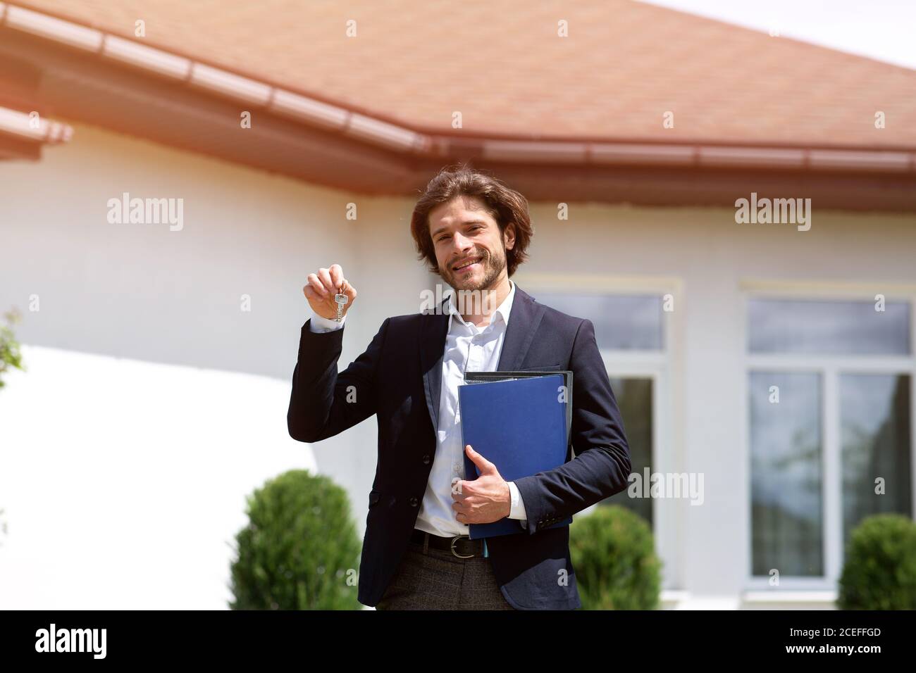 Fröhlicher Immobilienmanager mit Dokumenten, die Schlüssel zum neuen Haus halten Im Freien Stockfoto