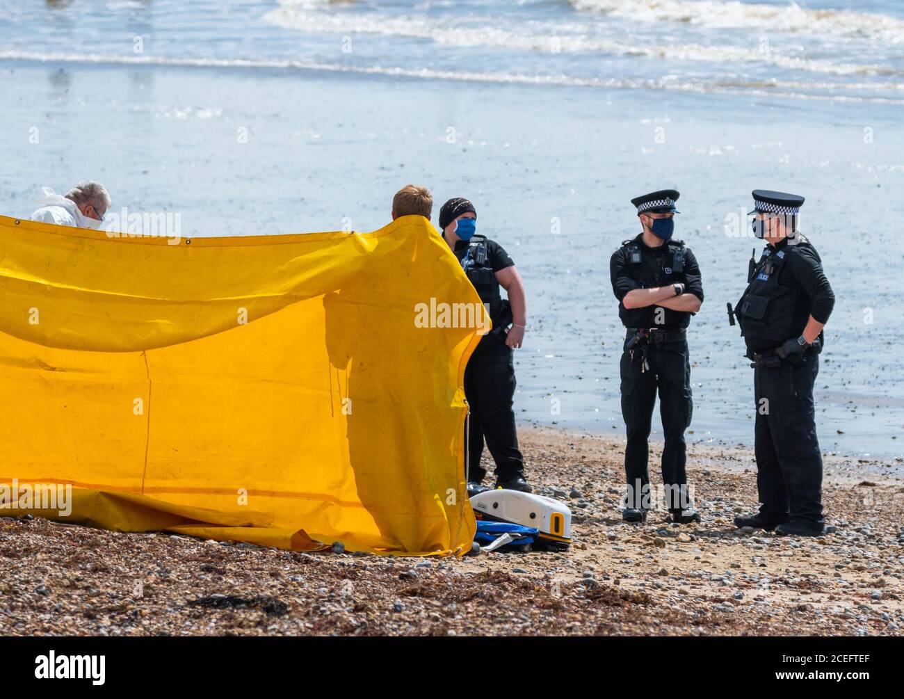 Polizei bei einem Vorfall an einem Strand in England, Großbritannien, mit einem Bildschirm für die Privatsphäre & Offiziere tragen Gesichtsmasken wegen der COVID19 Coronavirus Pandemie. Stockfoto