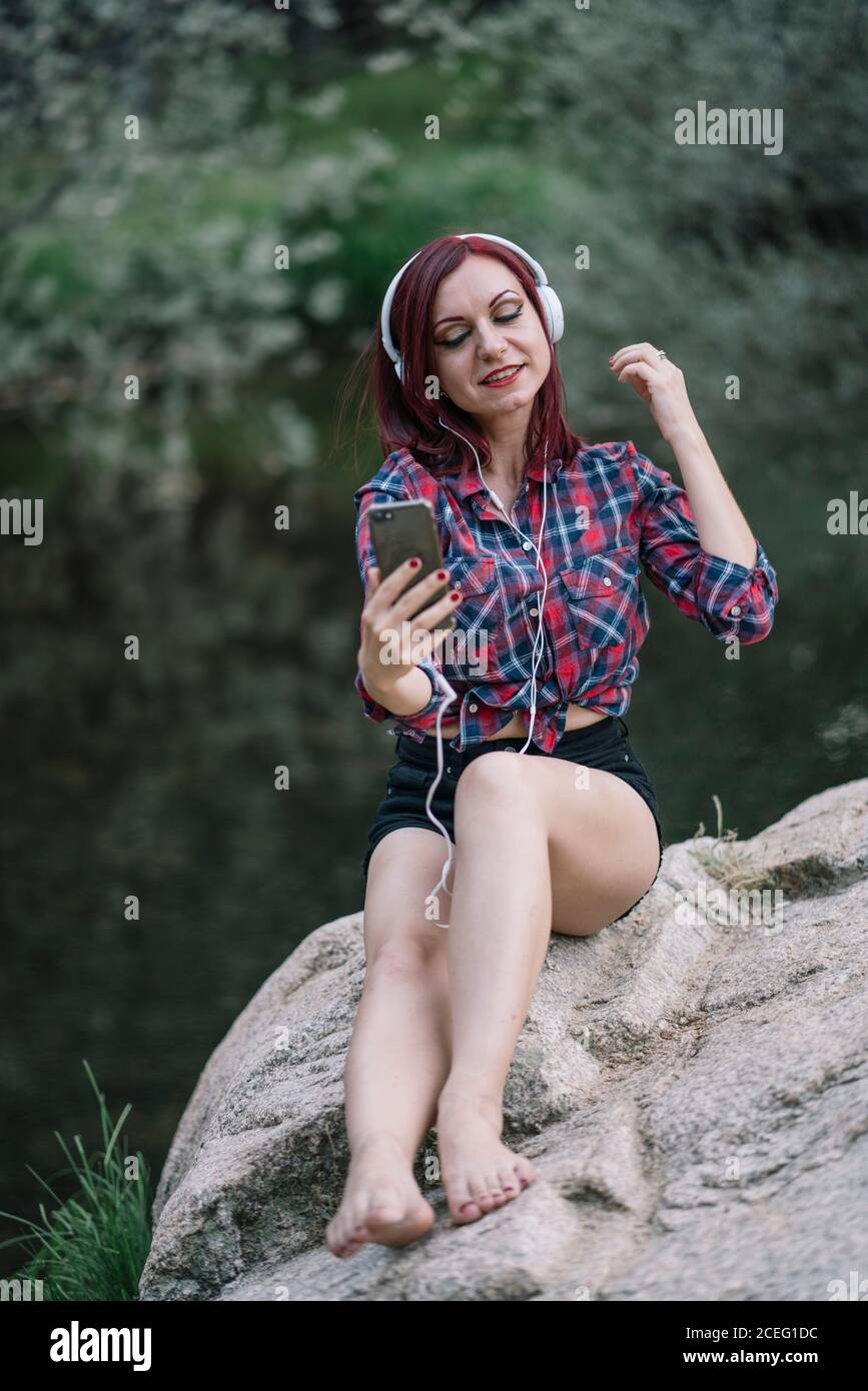 Ziemlich rothaarige Mädchen hört Musik am Fluss. Stockfoto
