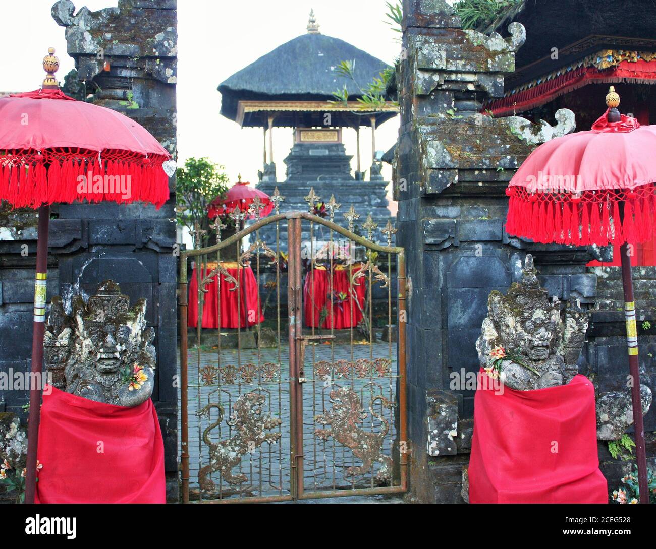Balinesische Statuen mit rotem Tuch unter roten Schirmen in bedeckt Vor dem Tor eines balinesischen Tempels Stockfoto