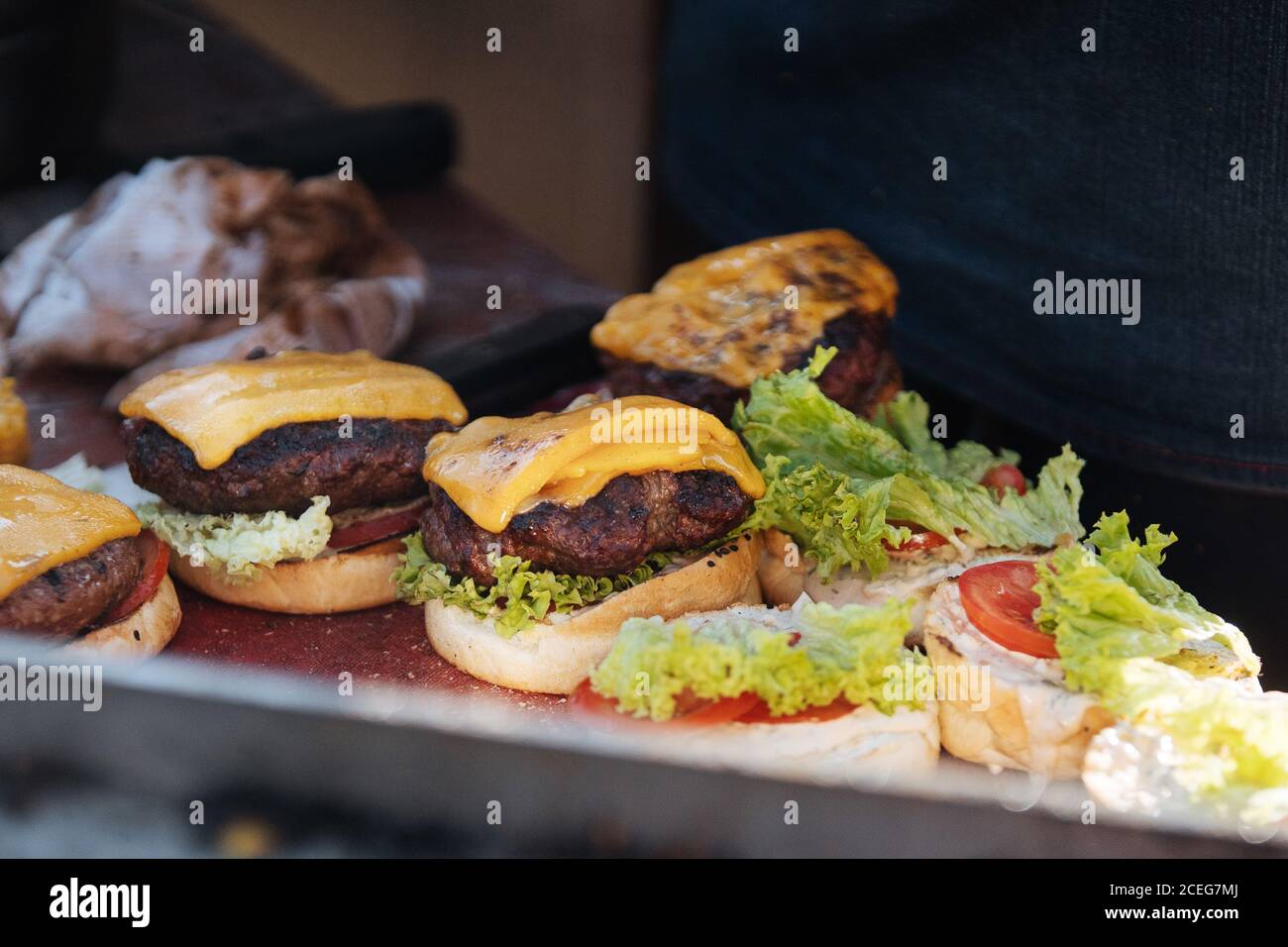 Gesichtsloser Schuss Koch in Handschuhen anordnen Brötchen mit frischen Gemüse- und Fleischpasteten mit Käseburgern Stockfoto