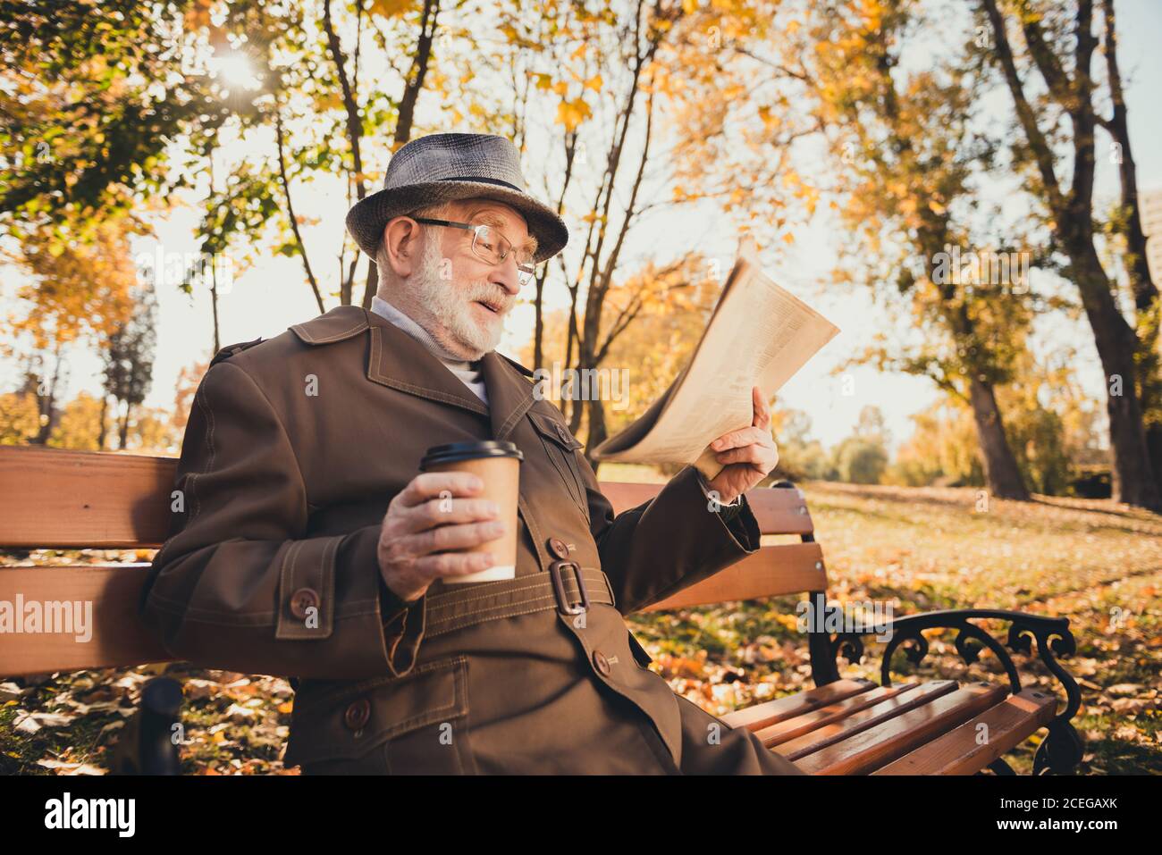 Profil Seitenfoto von aufgeregt alten Mann Rentner Ruhe entspannen Herbstpark vor der Tür haben Pause halten Takeout Kaffee Getränk Mug lesen unglaubliche Nachrichten Stockfoto