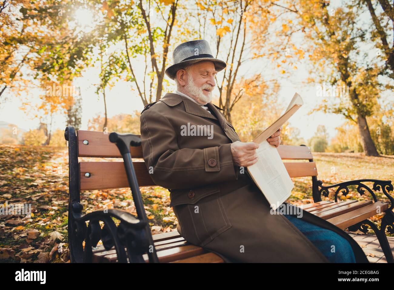 Profilseitenfoto des alten Mannes haben Morgen pensionierten Spaziergang Sitzen Fall Park Bank draußen lesen Stadtzentrum News Wear Kopfbedeckung mit langem Mantel Stockfoto