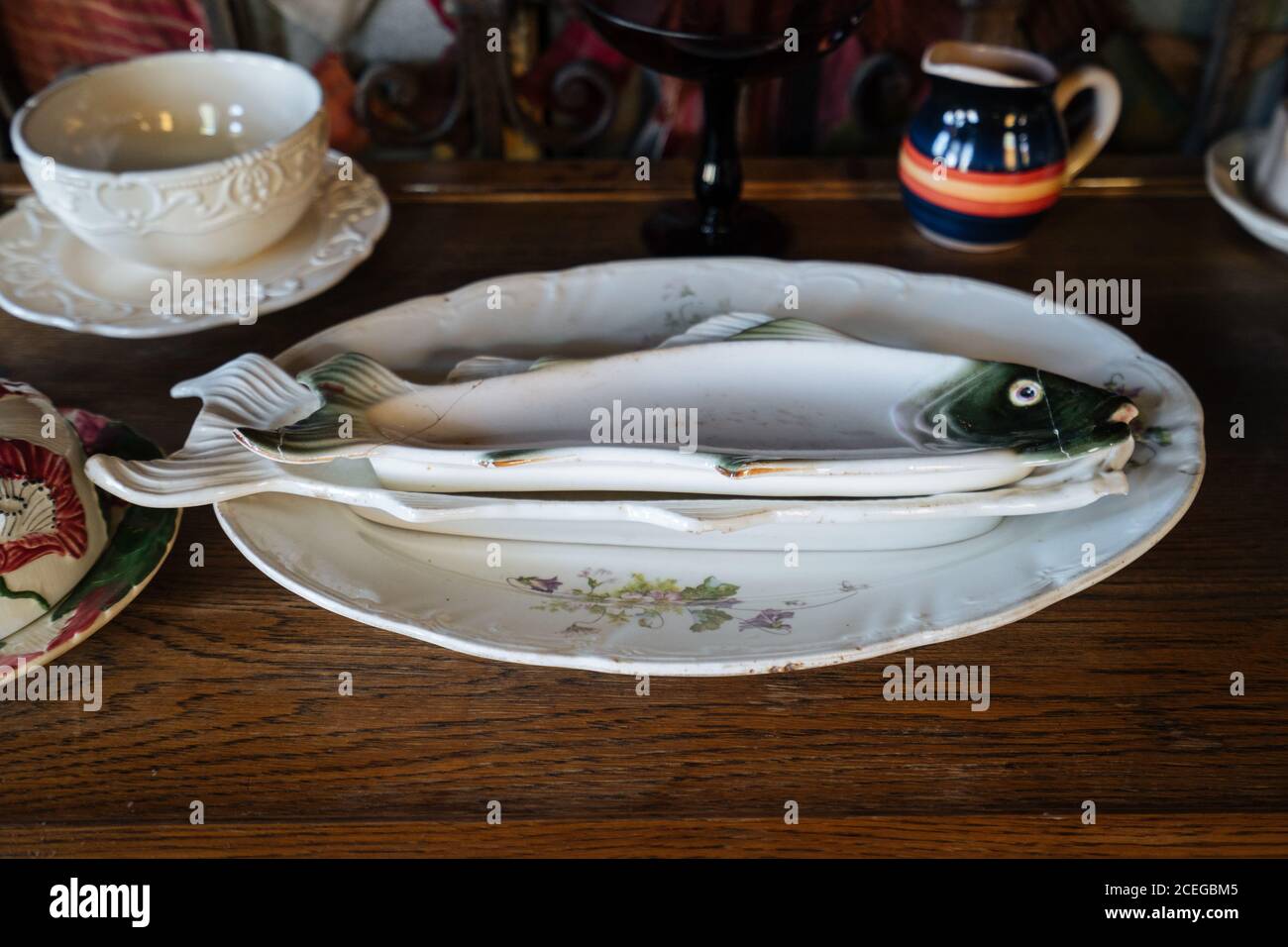 Shabby weißes Porzellan serviert Fischgerichte liegen auf großen runden Teller mit Blumenschmuck auf Holztisch mit Tasse mit Untertasse und Krug herum Stockfoto