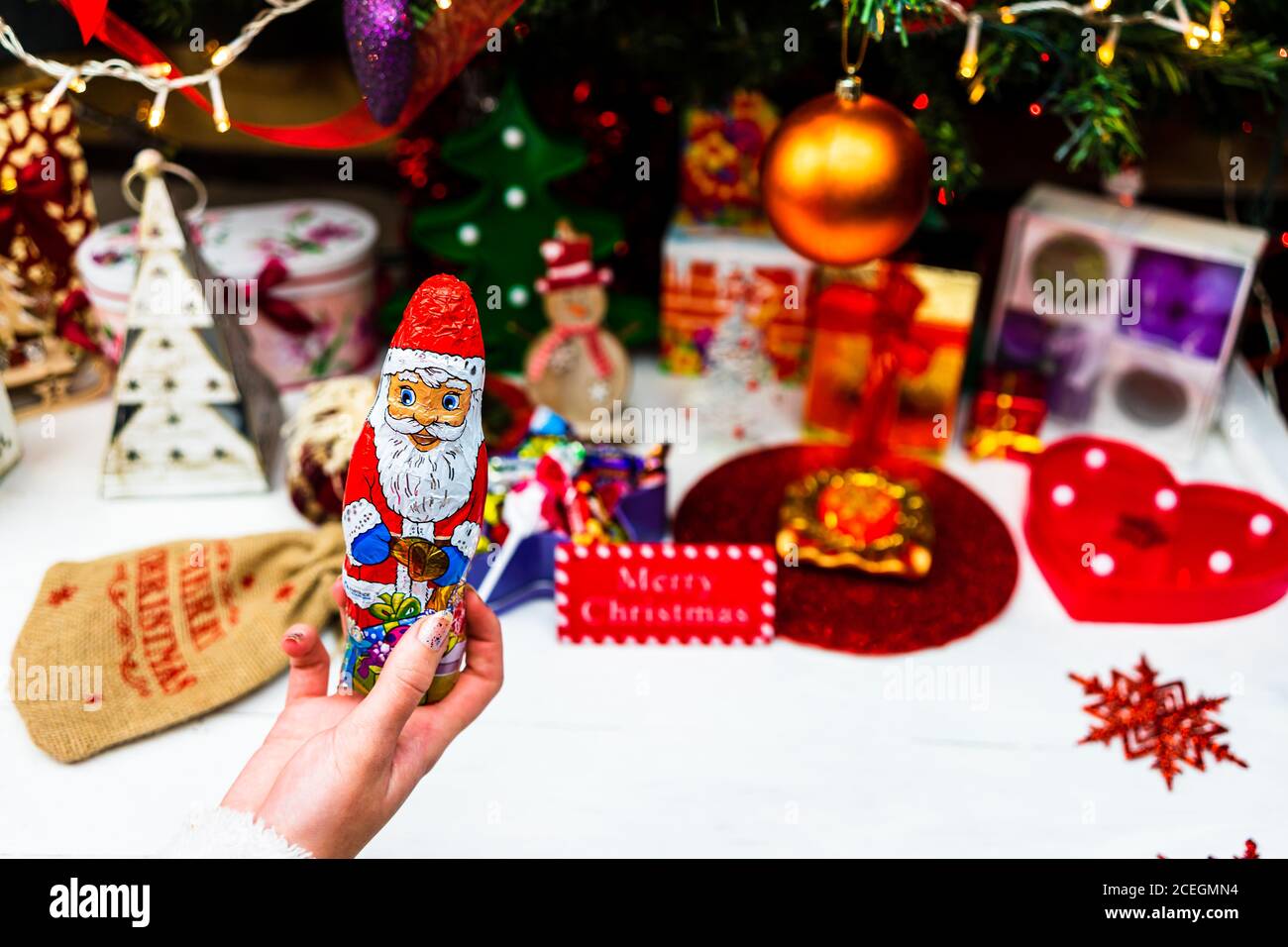 Hand hält die Weihnachtsmann-Schokoladenfigur vor dem Weihnachtsbaum. Dekorieren Christmass Baum isoliert Stockfoto