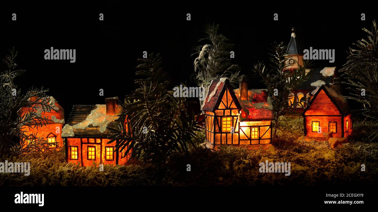 Panorama-Szene der Miniatur-Weihnachtslandschaft mit beleuchteten winzigen Keramikhäusern. Realistische hausgemachte Weihnachten Modell, Nachtdorf mit Bäumen und gefälschten Schnee. Stockfoto
