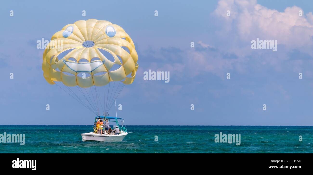 Gelber Flügel mit glücklichen Gesicht vom Fallschirmspringen gezogen von einem Boot. Sommer maritime Erholung Stockfoto