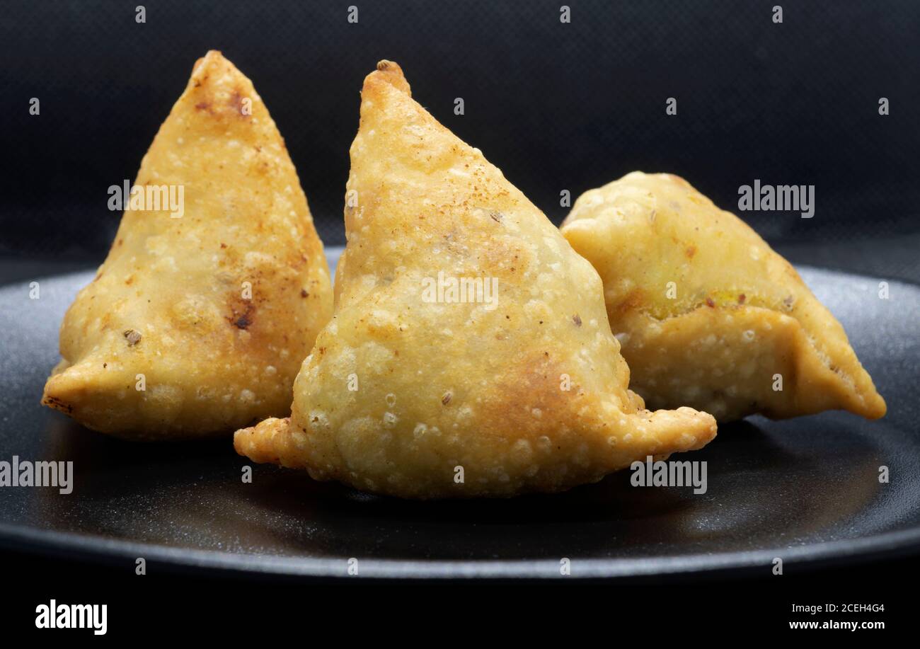 Drei goldbraune Samosas auf einem schwarzen Teller. Beliebter indischer Snack. Stockfoto
