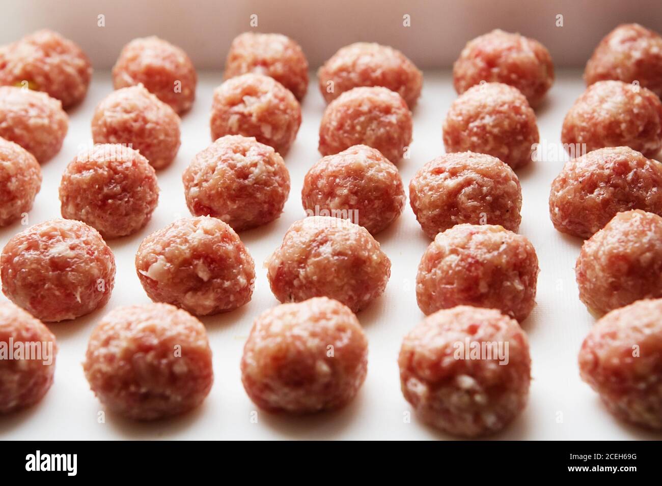 Frisch gekochte rohe Fleischbällchen liegen auf einem weißen Plastikküchenbrett. Stockfoto