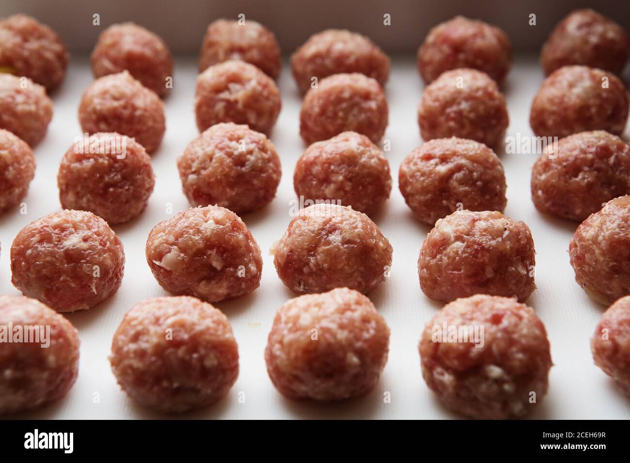 Frisch gekochte rohe Fleischbällchen liegen auf einem weißen Plastikküchenbrett. Stockfoto