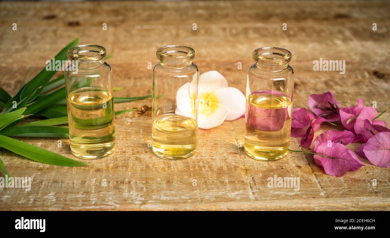 Ätherisches Öl in drei kleinen Glasflaschen mit Bambusblättern, Bougainvillea und Frangipani Blumen auf Holzgrund. Selektiver Fokus. Natürliche Cos Stockfoto