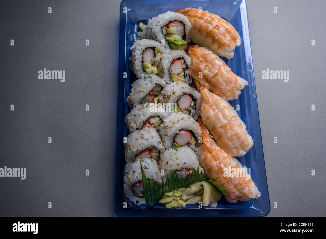 Plastikbehälter voller frisch gemachter Regenbogen Sushi Rolle aus Der Supermarkt mit Wasabi Ingwer und Sojasauce serviert Auf der Seite Stockfoto