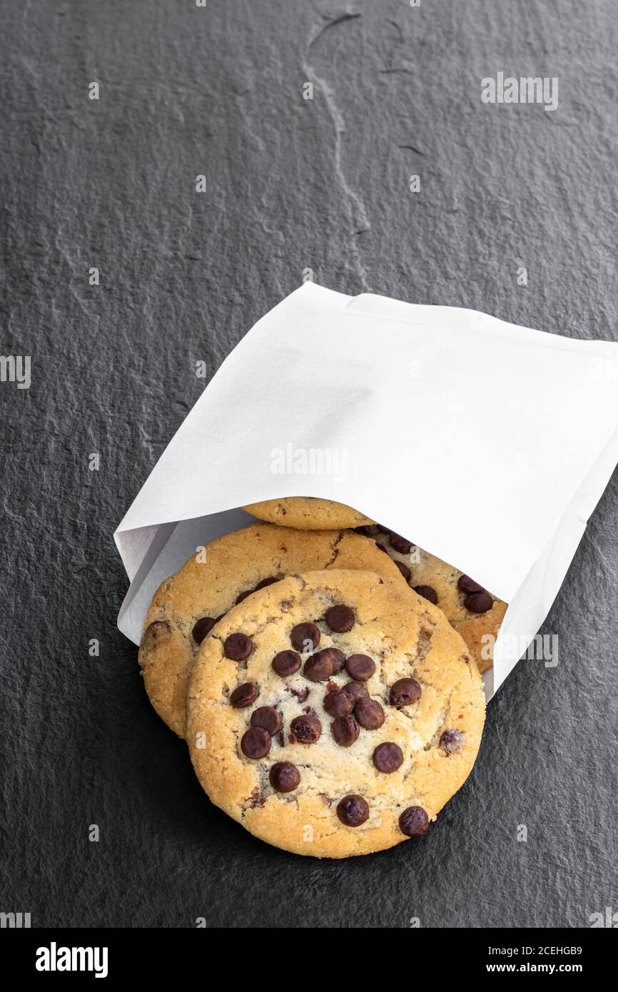 Chocolate Chip Cookies in weißem Papierbeutel auf schwarzem Stein Hintergrund Stockfoto