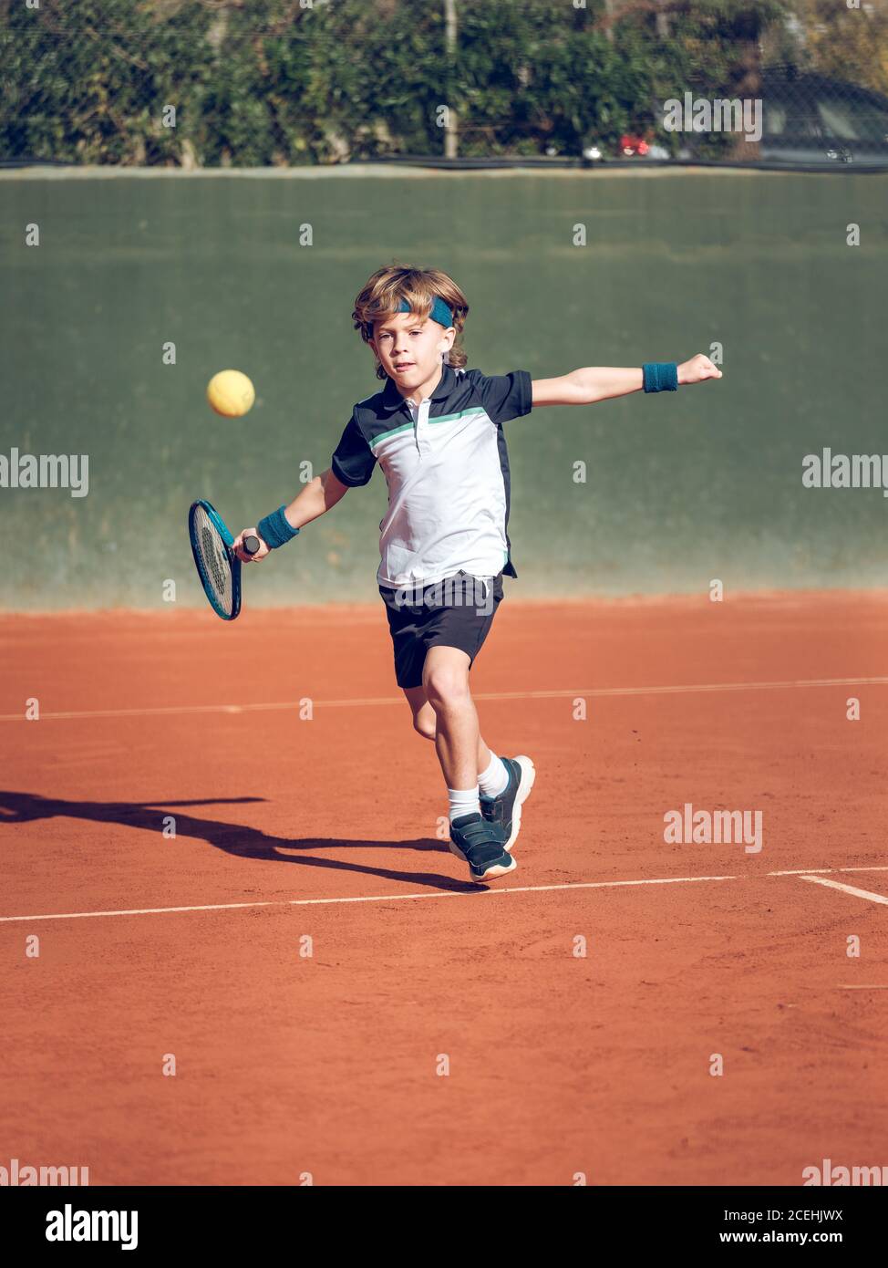 Kleines Kind in Sportbekleidung mit Tennisschläger versucht zu schlagen Schwebende Kugel in der Luft auf dem Platz an sonnigen Tag Stockfoto