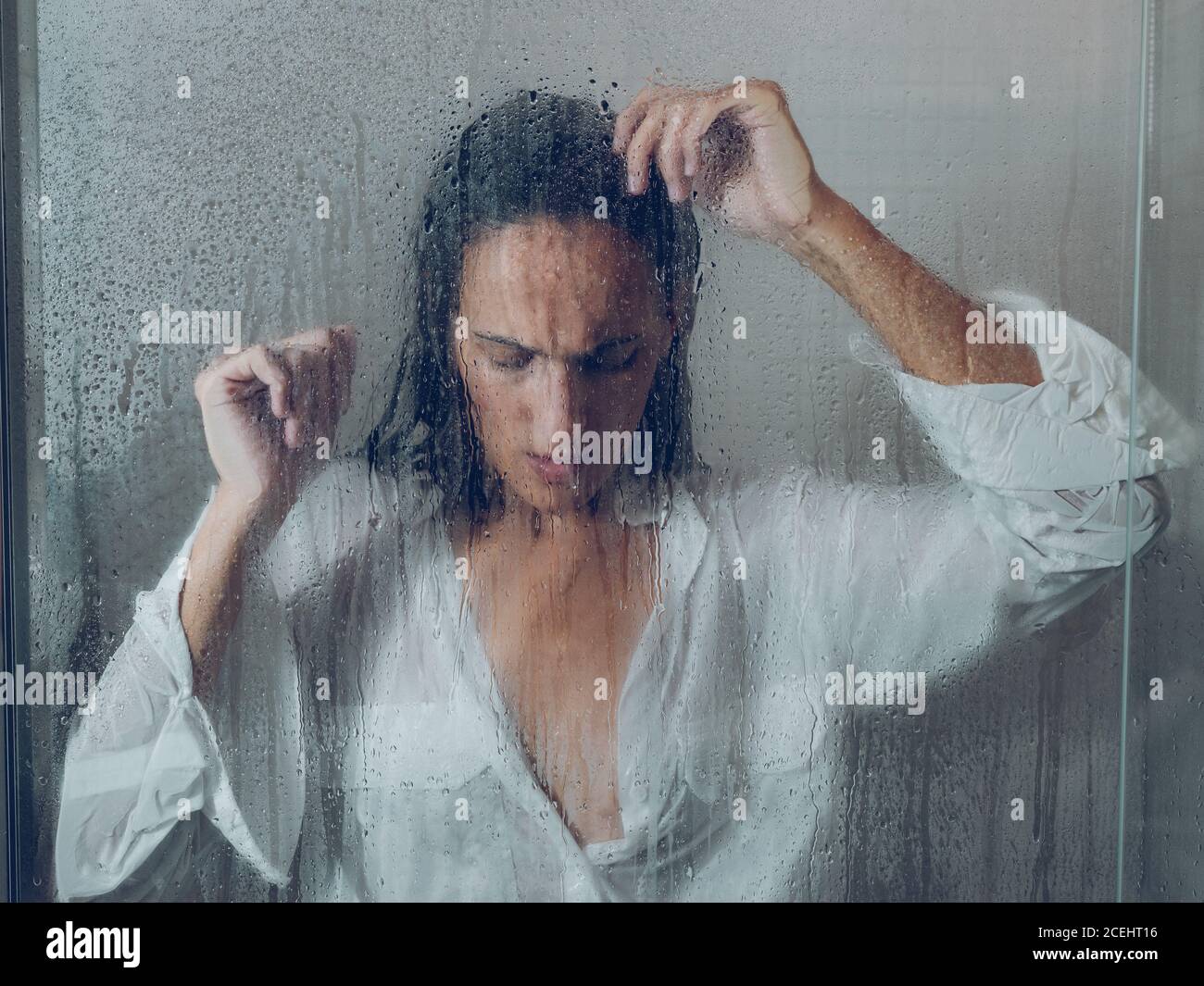 Attraktive junge Dame im weißen nassen Hemd neben Glas stehen Der Duschkabine Stockfoto