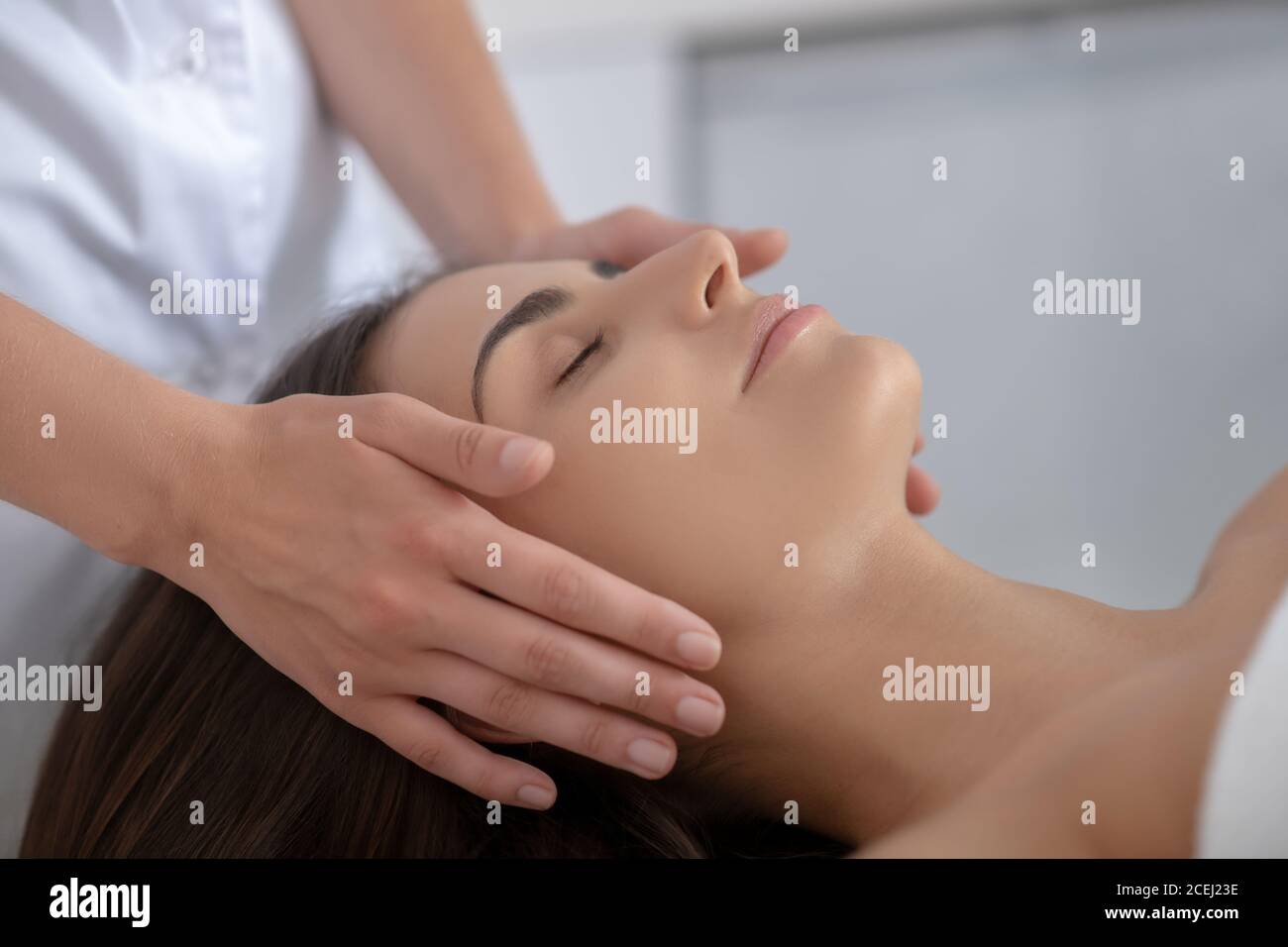 Junge hübsche Frau liegend und mit Gesichtsmassage Stockfoto