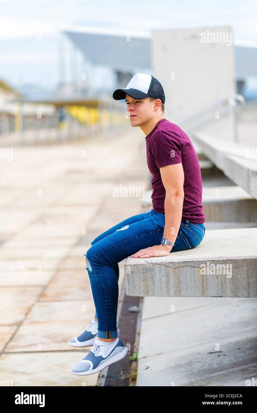 Seitenansicht eines Teenagers in legerer Kleidung während des Sitzens Auf einer Bank im Freien und wegschauen Stockfoto
