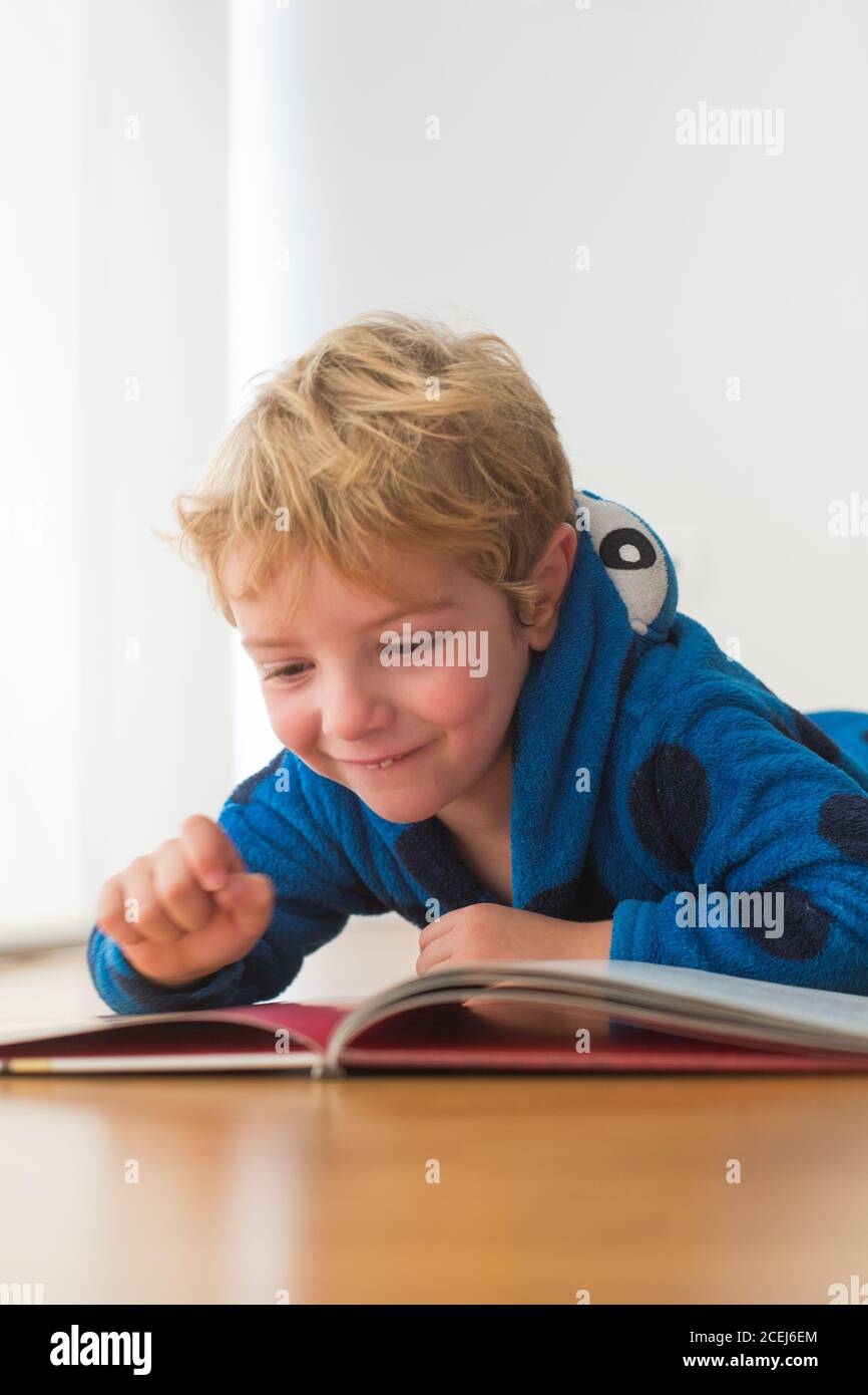 Kaukasische blonde Junge liest ein Buch auf einem Holzboden Stockfoto