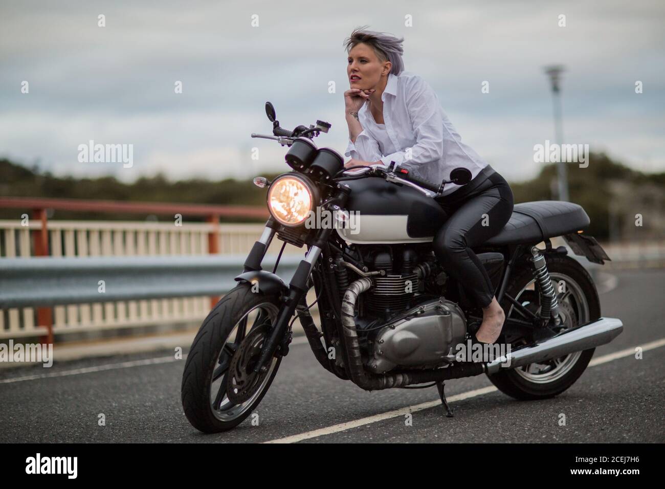 Attraktive junge Frau sitzt auf ihrem Cafe Racer Motorrad Stockfoto