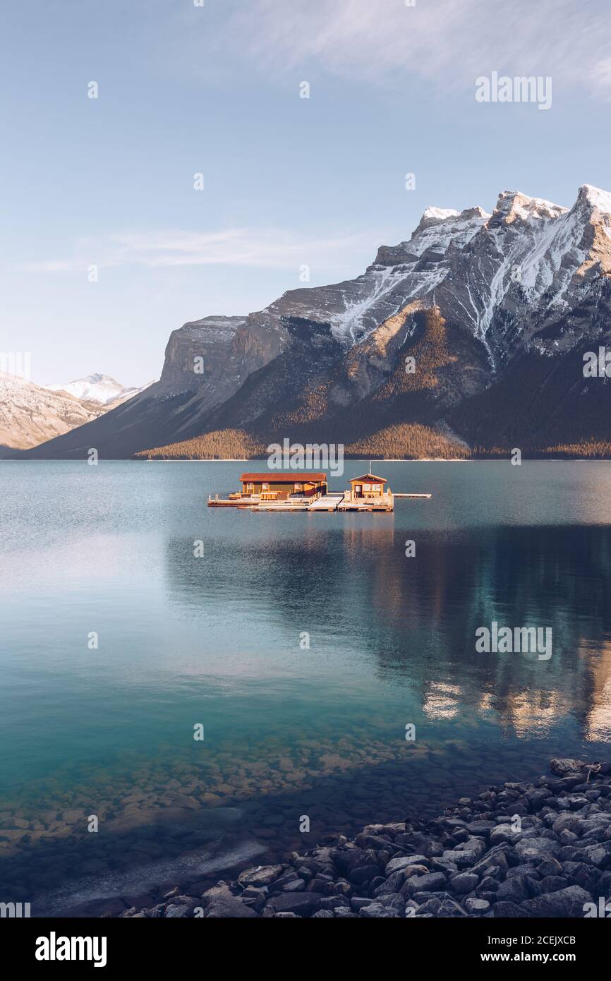 Gebäude mit braunem Dach unter Sonnenschein mitten im Hochland see mit klarem blauen Wasser im Hintergrund mit malerischen Bergen Und Wald Stockfoto